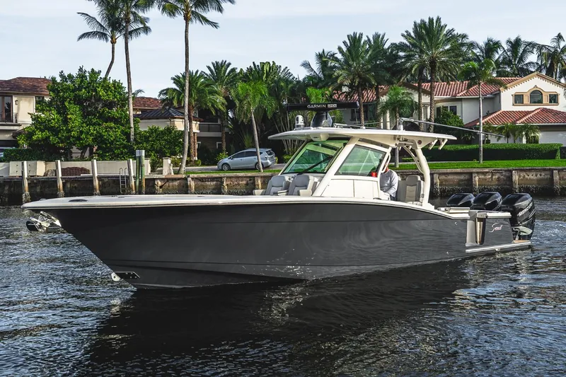 Slide: The Image of 2021 Scout 355 LXF boat cruising on a scenic waterfront with palm trees. - 15
