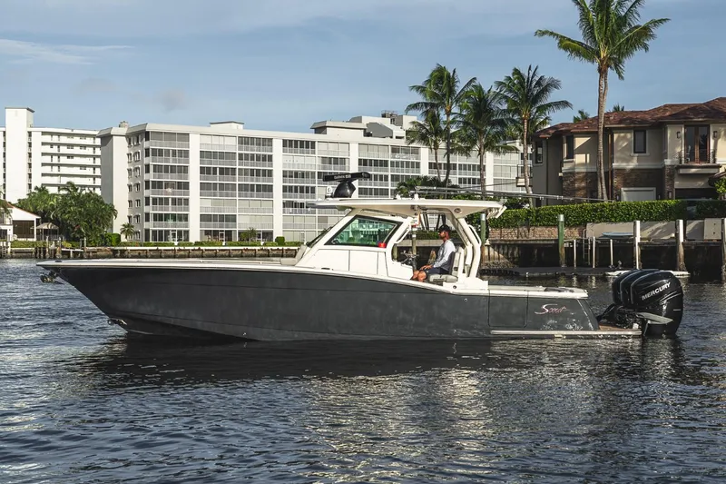 Slide: The Image of 2021 Scout 355 LXF boat cruising near waterfront buildings and palm trees. - 2