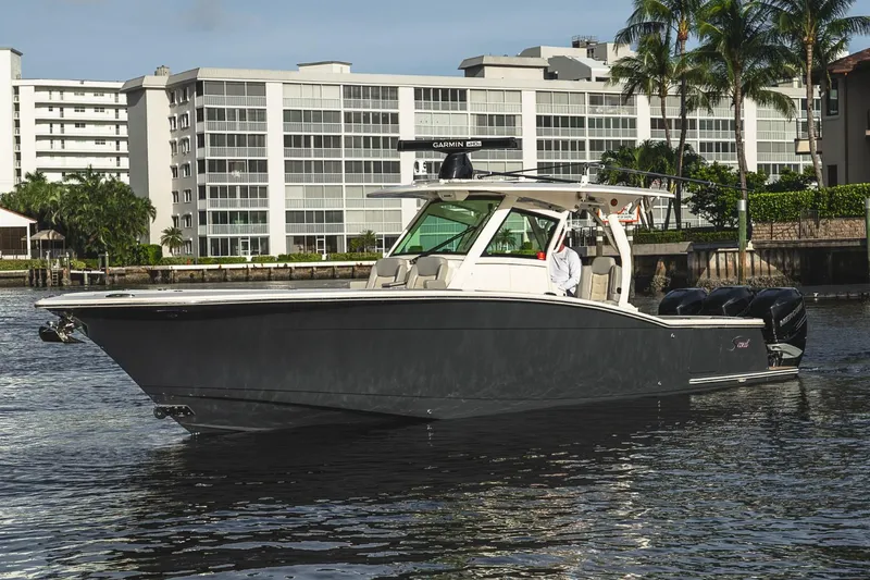 Slide: The Image of 2021 Scout 355 LXF boat cruising near waterfront buildings and palm trees. - 3