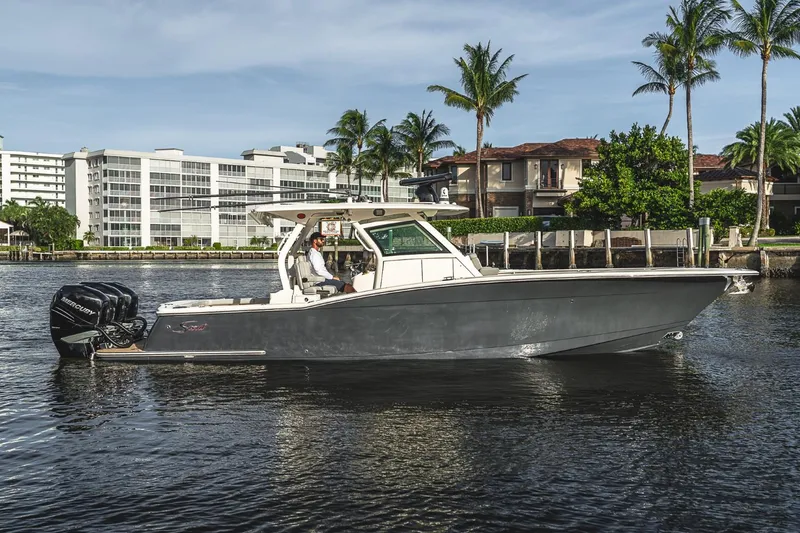 Slide: The Image of 2021 Scout 355 LXF boat cruising near waterfront homes and palm trees. - 6