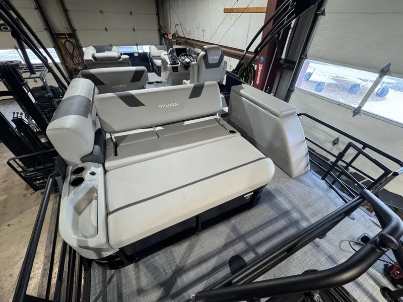 Slide: The Image of 2025 Sylvan L3 CLZ pontoon boat interior with gray seating and cup holders in a garage. - 10