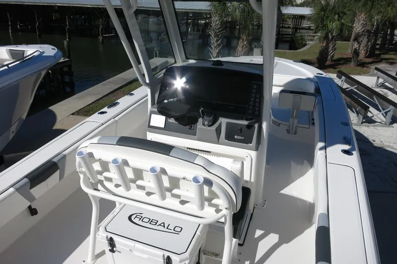 Slide: The Image of 2025 Robalo 266 Cayman boat interior with console and seating, docked near palm trees. - 13