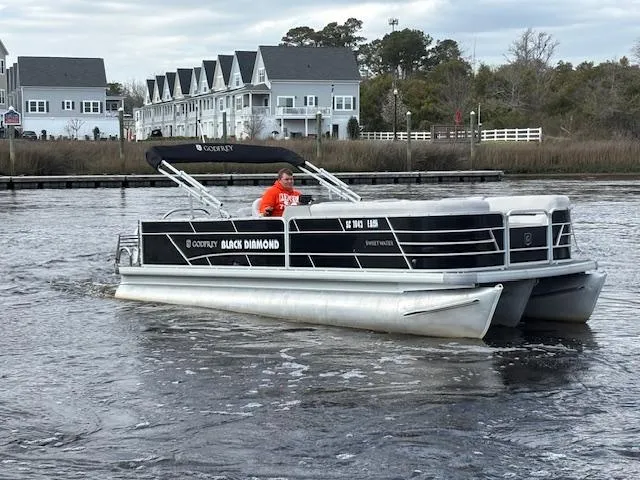 The Image of 2022 Sweetwater 2286 pontoon boat cruising on a river near residential area. - 1
