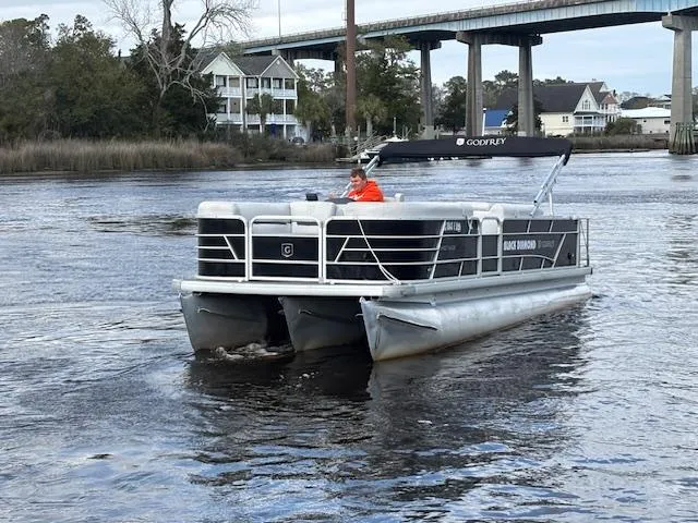 Slide: The Image of 2022 Sweetwater 2286 pontoon boat cruising on a river near a bridge and houses. - 6