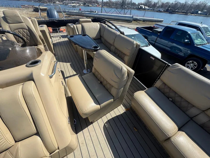 Slide: The Image of 2016 Bennington 2275 RCW pontoon boat with beige seating and table, docked near a blue truck. - 10