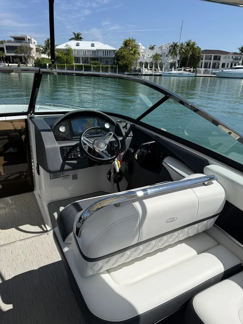 Slide: The Image of 2019 Regal 29 OBX boat interior with steering wheel, white seating, and waterfront view. - 23
