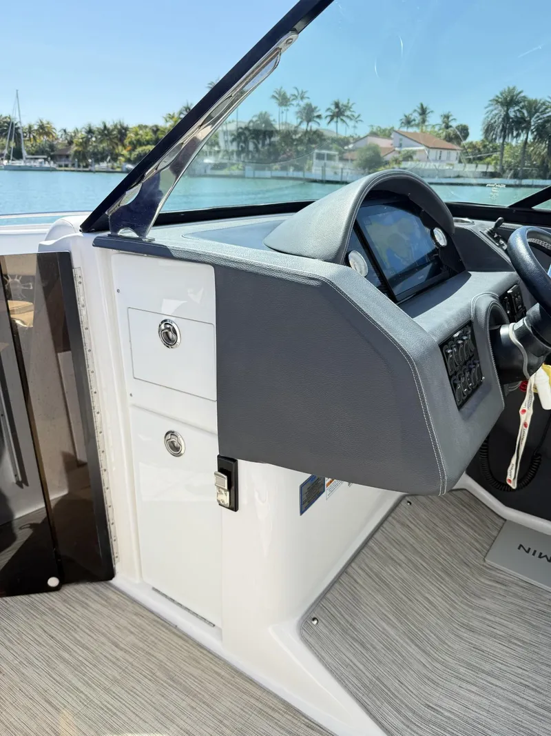 Slide: The Image of 2019 Regal 29 OBX boat dashboard with steering wheel and control panel, docked by palm trees. - 25