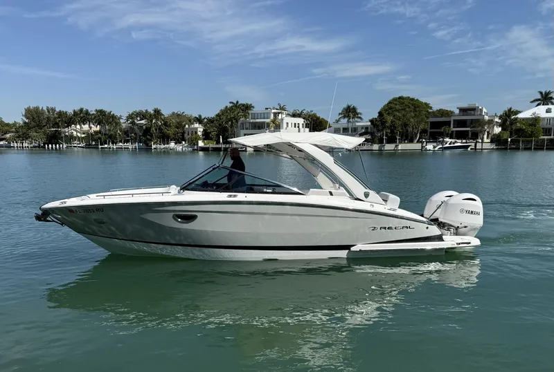 Slide: The Image of 2019 Regal 29 OBX boat cruising on calm water with scenic waterfront homes in the background. - 7