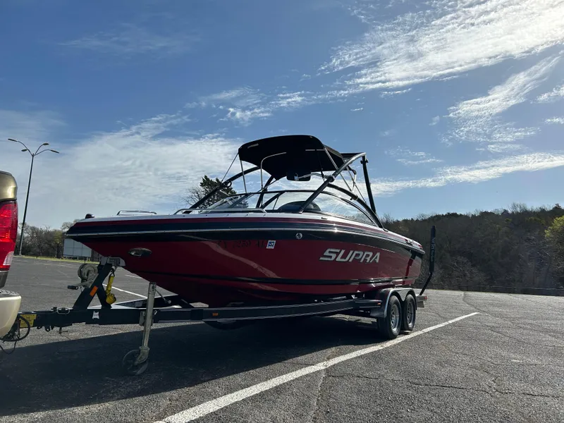 Slide: The Image of 2007 Supra Sunsport 22 V boat on trailer in parking lot, red and black design. - 2