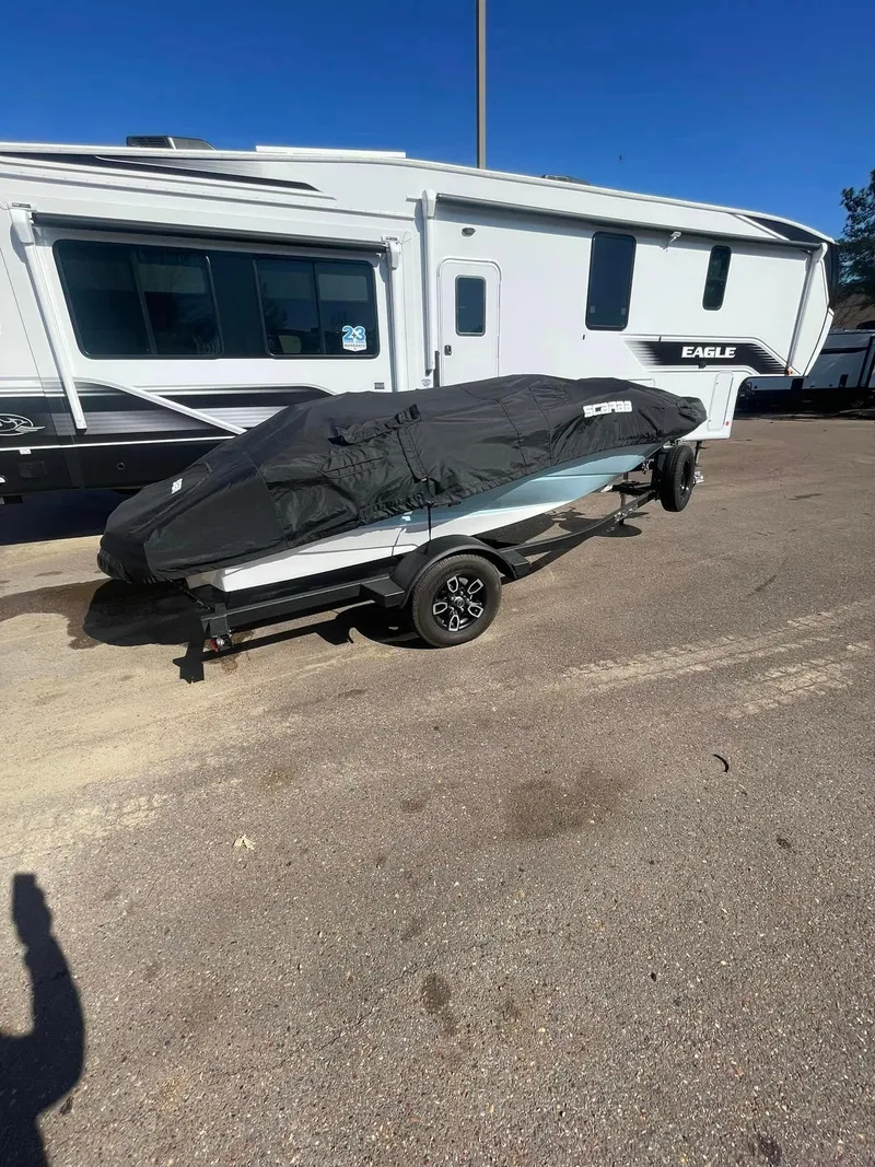 Slide: The Image of 2022 Scarab 165 SE boat covered on trailer, parked beside RV. - 1