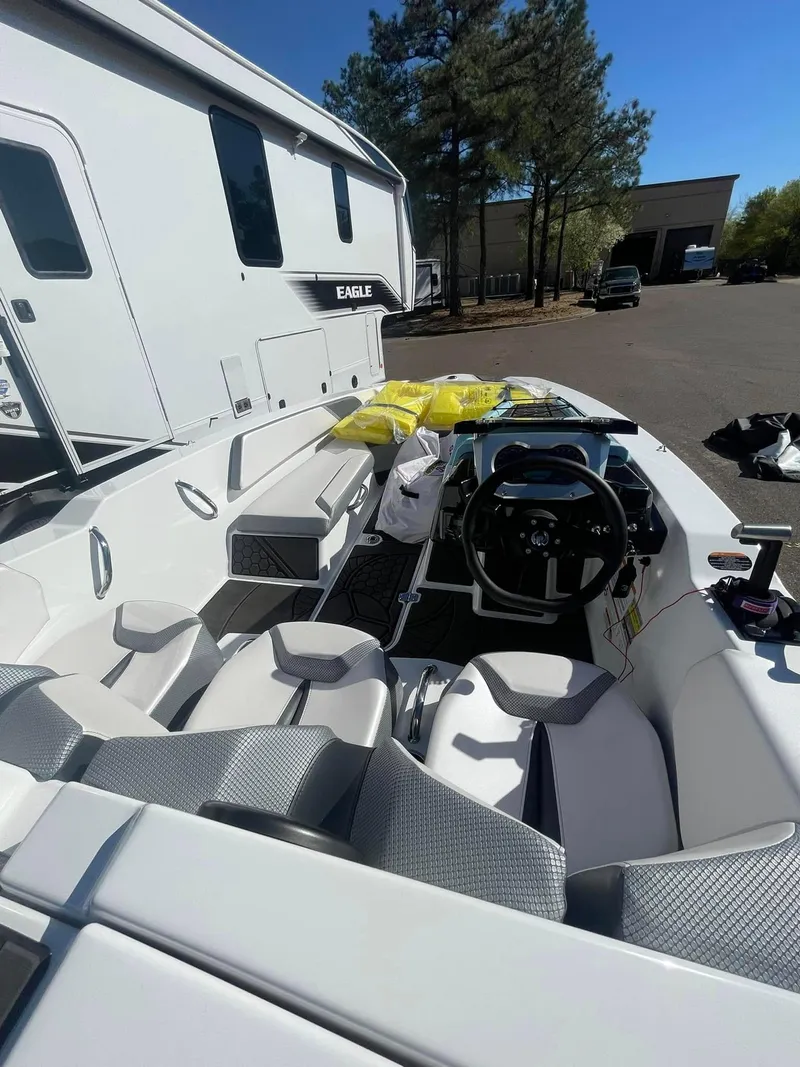 Slide: The Image of 2022 Scarab 165 SE boat interior with modern seating and steering, parked near RV. - 2
