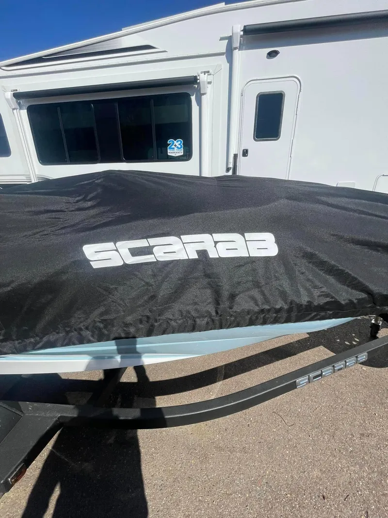 Slide: The Image of 2022 Scarab 165 SE boat covered, parked beside a white trailer. - 7