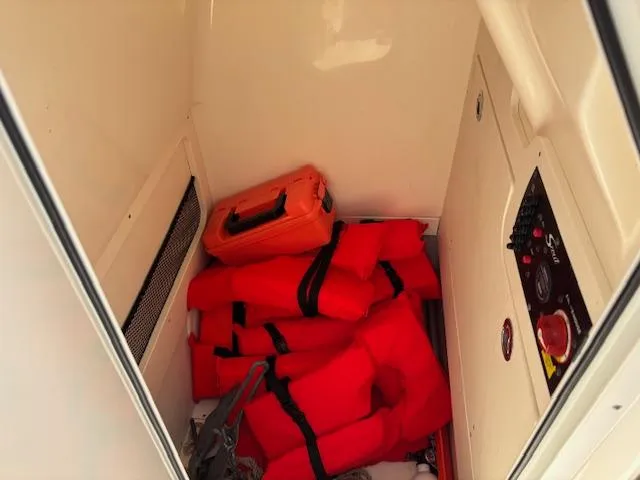 Slide: The Image of Storage compartment with red life jackets and orange case on a 2022 Scout 215 XSF boat. - 34