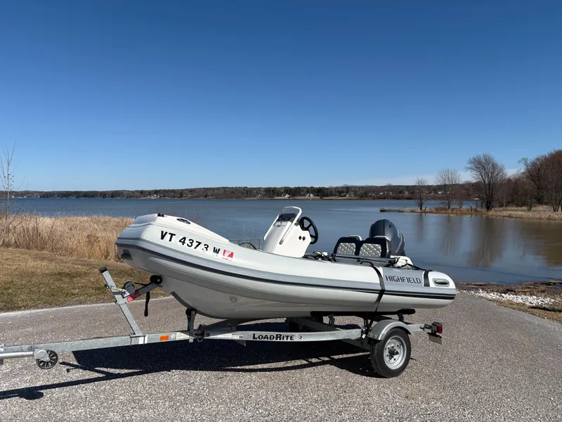 Slide: The Image of 2023 Highfield Sport 360 boat on trailer by a lake under clear blue sky. - 0