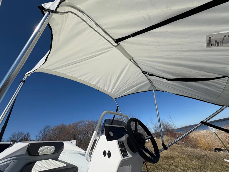 Slide: The Image of 2023 Highfield Sport 360 boat with canopy, steering wheel, and seating, under clear blue sky. - 18