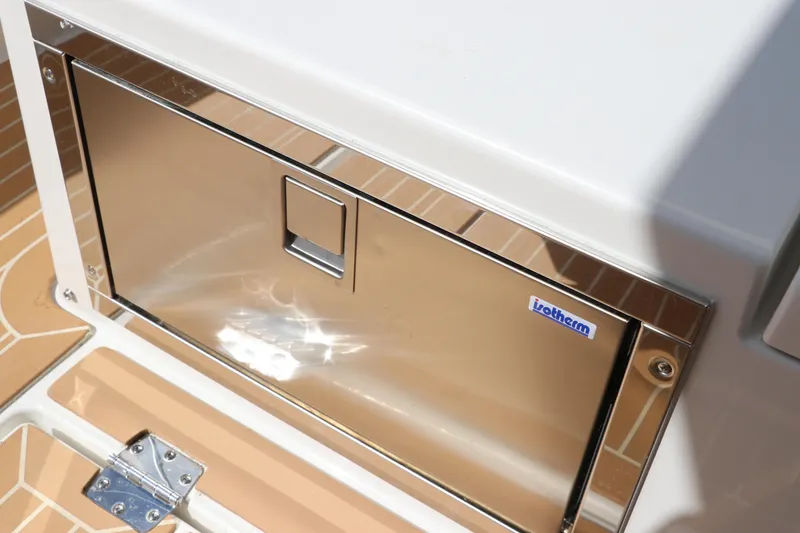 Slide: The Image of 2025 Nimbus Tender 8 boat interior with red seating and wooden table, near lush shoreline. - 27