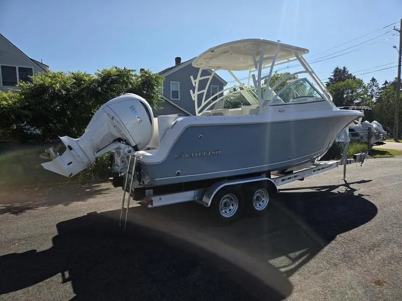 Slide: The Image of 2025 Sailfish 245 DC boat on trailer, parked outdoors in sunny setting. - 7