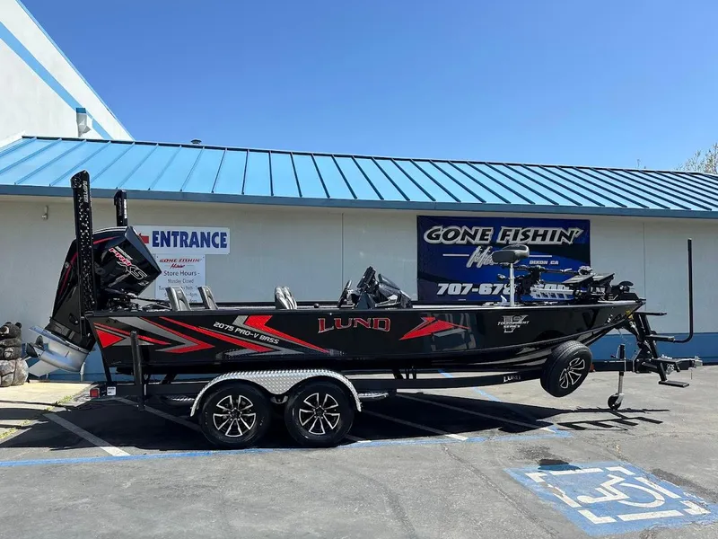 Slide: The Image of 2025 Lund 2075 Pro-V Bass XS boat on trailer outside a fishing store. - 0