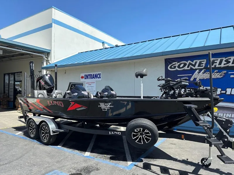 Slide: The Image of 2025 Lund 2075 Pro-V Bass XS boat on trailer outside a fishing store. - 1