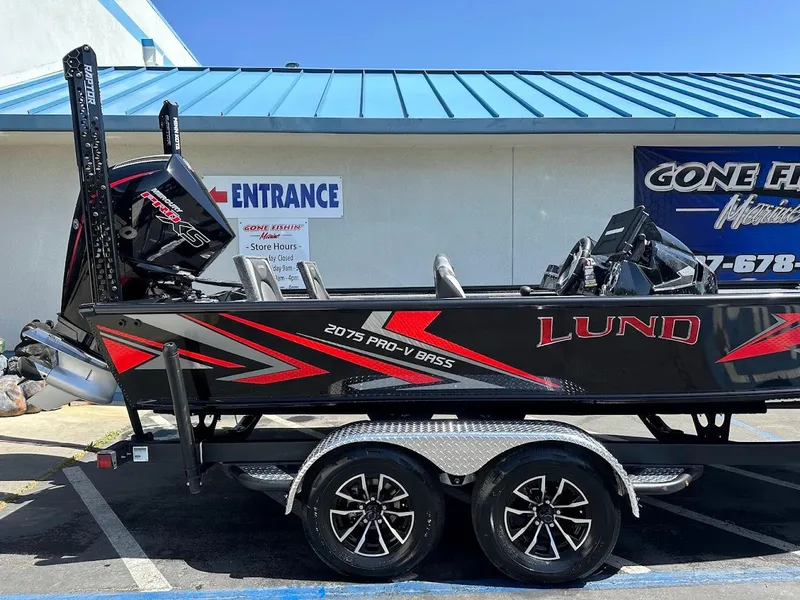 Slide: The Image of 2025 Lund 2075 Pro-V Bass XS boat on trailer, parked outside a marine store. - 5