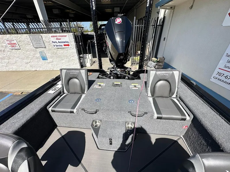 Slide: The Image of 2025 Lund 2075 Pro-V Bass XS boat interior with seating and motor, parked outdoors. - 9