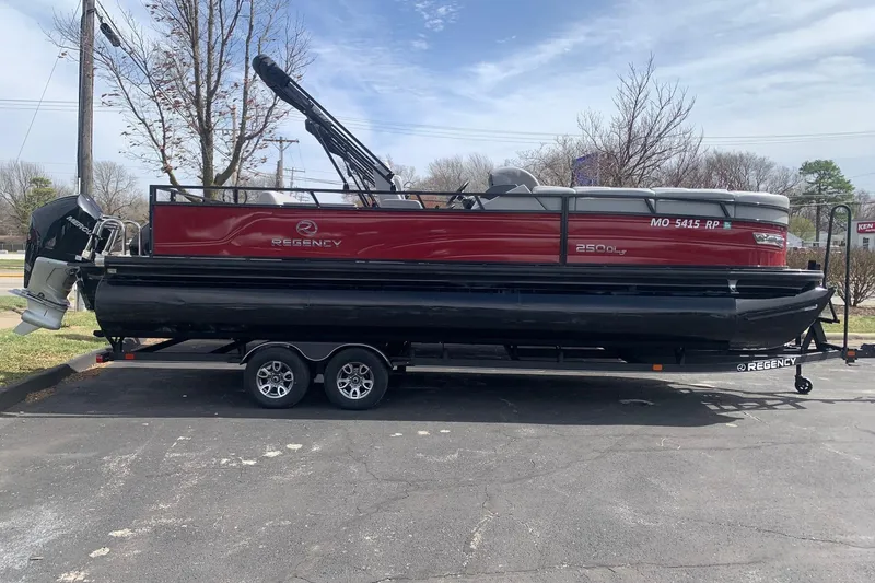 Slide: The Image of 2024 Regency R250DL3 pontoon boat on trailer, red and black design, parked outdoors. - 0