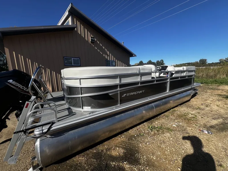 Slide: The Image of A 2025 Starcraft LX 22 R pontoon boat is on dry land next to a building. - 1