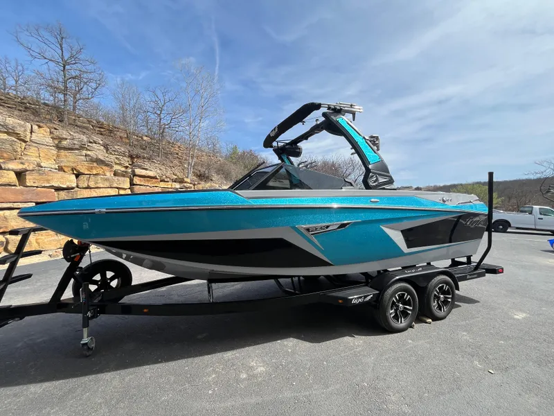 Slide: The Image of 2023 Tigé 22RZX boat in vibrant blue on a trailer, parked outdoors. - 2