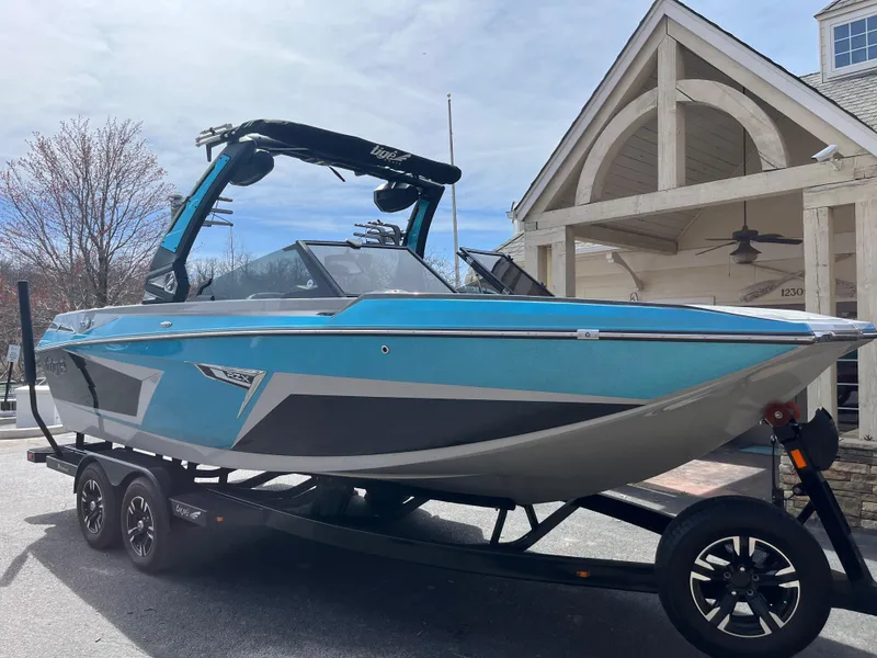 Slide: The Image of 2023 Tigé 22RZX boat in blue and gray on a trailer, parked near a building. - 3