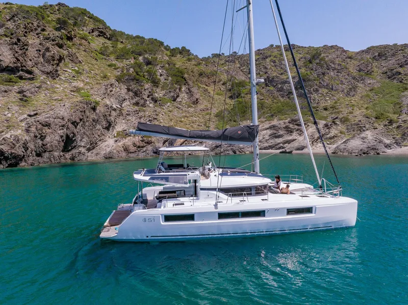 Slide: The Image of 2025 Lagoon 51 ICONIC catamaran sailing in clear turquoise waters near rocky coastline. - 14