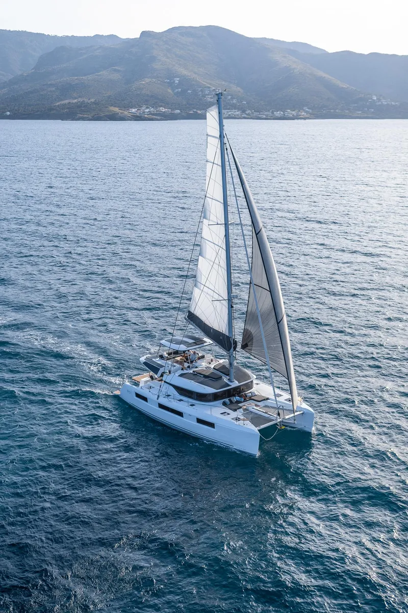 Slide: The Image of 2025 Lagoon 51 ICONIC catamaran sailing on open sea with mountainous backdrop. - 18