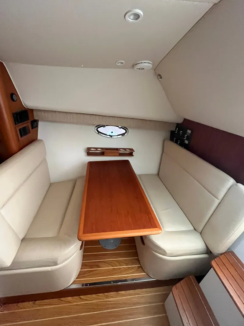 Slide: The Image of 2004 Tiara Yachts Classic interior with wooden table, beige seating, and porthole window. - 3