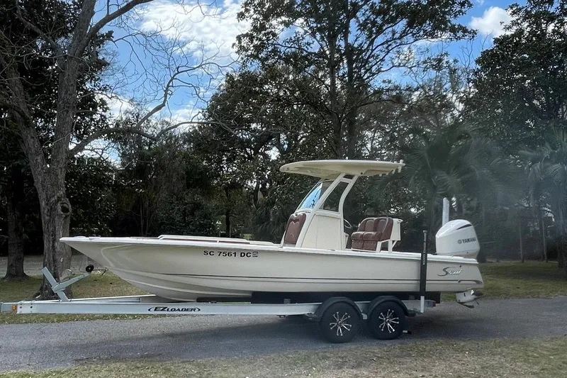 Slide: The Image of 2015 Scout 251 XS boat on trailer, parked outdoors with trees in the background. - 2