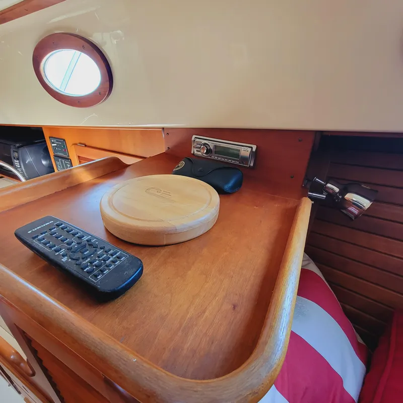 Slide: The Image of 1999 Hinckley Picnic Boat Classic interior with remote, wooden tray, and porthole window. - 21