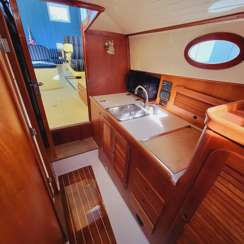 Slide: The Image of 1999 Hinckley Picnic Boat Classic interior with wooden cabinetry and compact kitchen area. - 22