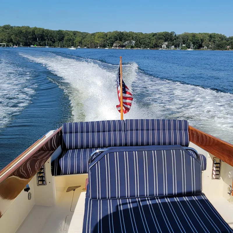 Slide: The Image of 1999 Hinckley Picnic Boat Classic cruising on a lake with striped seating and American flag. - 8