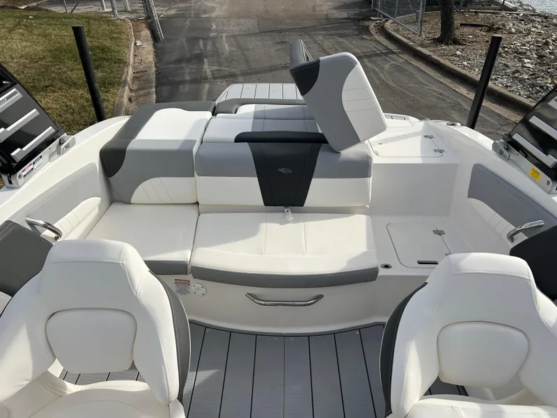 Slide: The Image of 2025 Chaparral 21 SSi boat interior with white and gray seating, docked by a lakeside. - 15