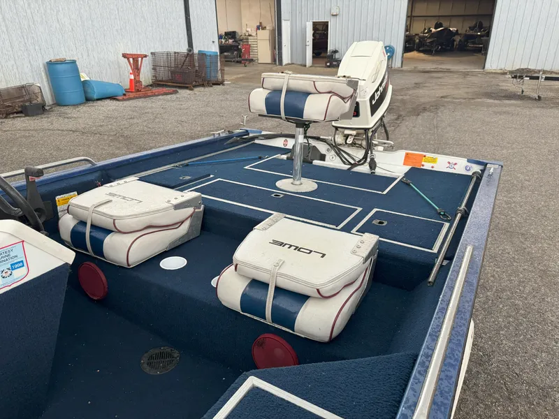 Slide: The Image of 1994 Lowe 170 boat interior with blue and white seating, docked near a warehouse. - 10