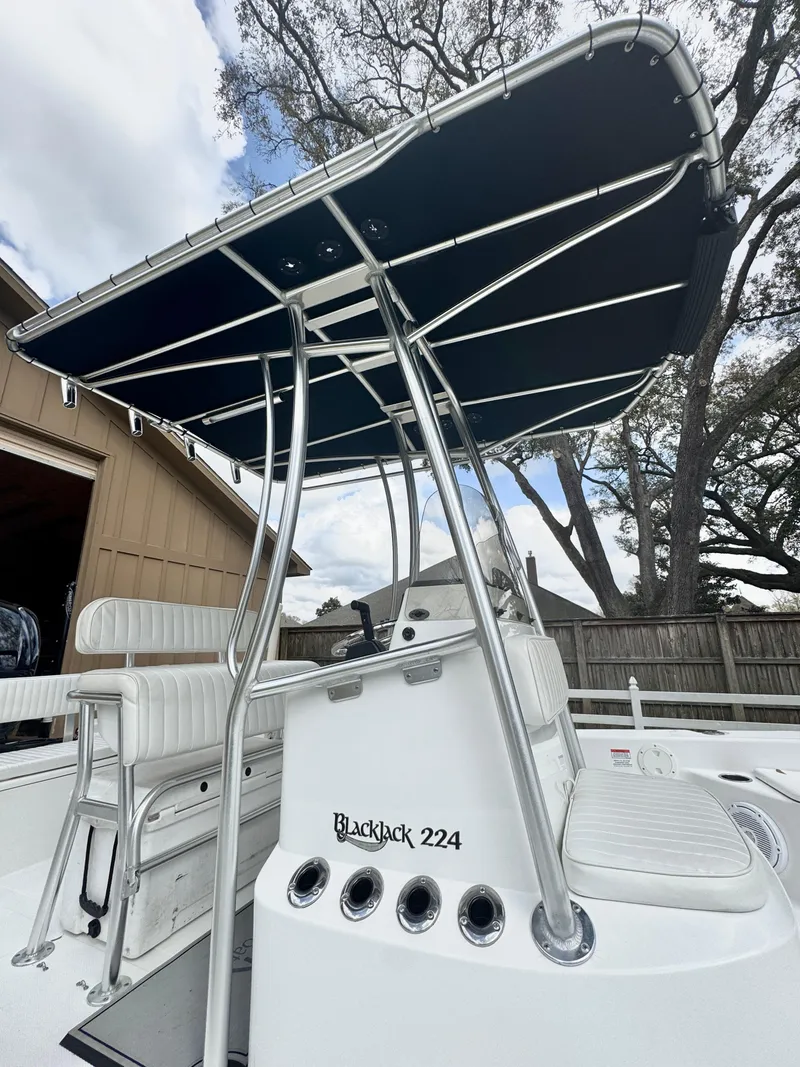 Slide: The Image of 2011 BlackJack 224 boat with T-top, white seating, and sleek design in a yard setting. - 21