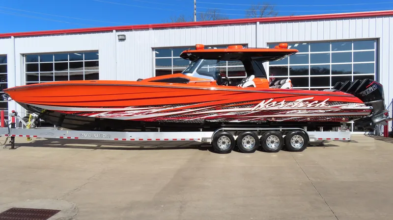 The Image of 2023 Nor-Tech 450 boat in vibrant orange on a trailer outside a garage. - 0