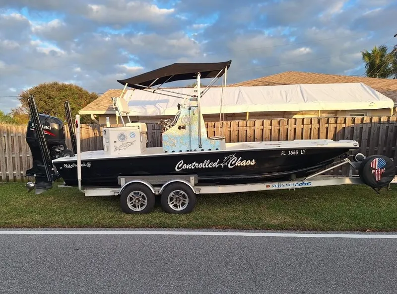 Slide: The Image of Bay Hawk 204 boat on trailer, 1992 model, named "Controlled Chaos," parked by a wooden fence. - 2