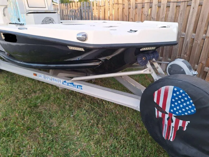 Slide: The Image of Bay Hawk 204 boat on trailer, American flag skull cover, wooden fence background. - 6