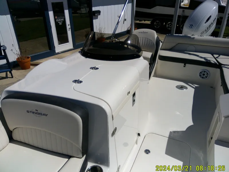 Slide: The Image of 2022 Stingray 212SC boat interior with seating and console, docked outdoors. - 15