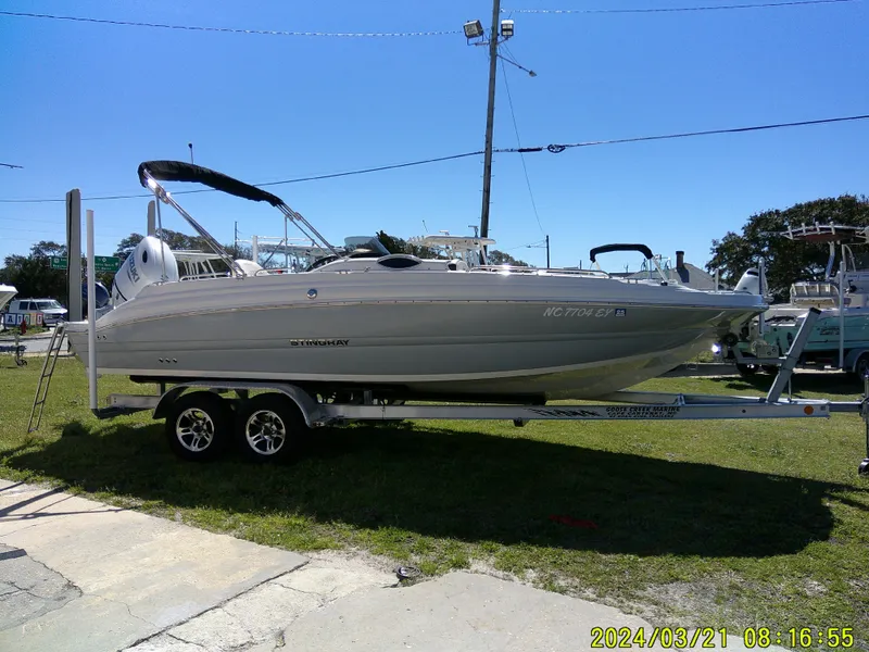 Slide: The Image of 2022 Stingray 212SC boat on trailer, parked outdoors under clear blue sky. - 2