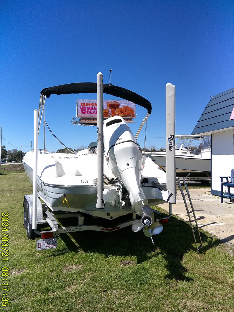 Slide: The Image of 2022 Stingray 212SC boat on trailer, parked outdoors under clear blue sky. - 4