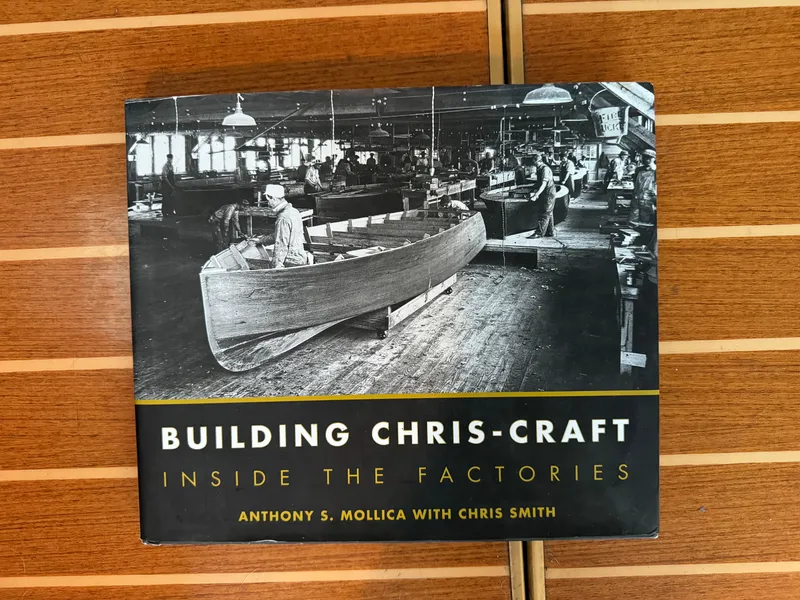 Slide: The Image of "Building Chris-Craft" book cover on wooden surface, featuring a vintage boat factory scene. - 36