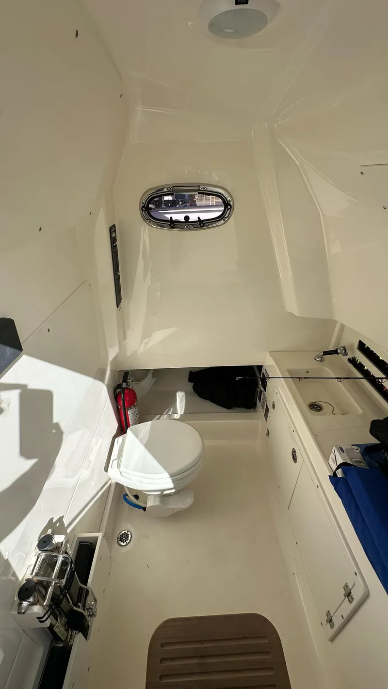 Slide: The Image of 2022 Boston Whaler 330 Outrage cabin interior with toilet and porthole window. - 15