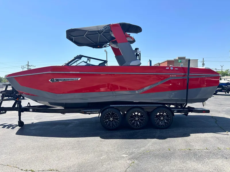 Slide: The Image of 2025 Nautique Super Air Nautique G25 boat, red and gray, on a trailer in a parking lot. - 13