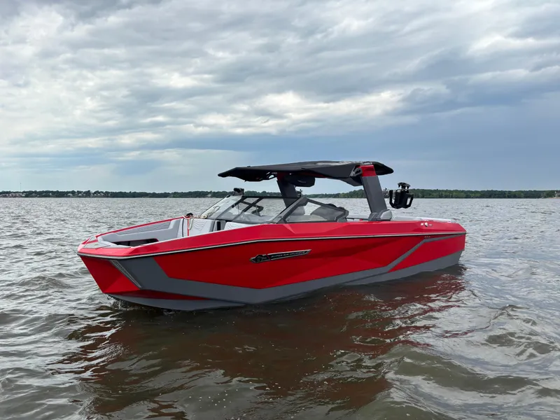 Slide: The Image of 2025 Nautique Super Air Nautique G25 boat on water, red and gray design, under cloudy sky. - 2