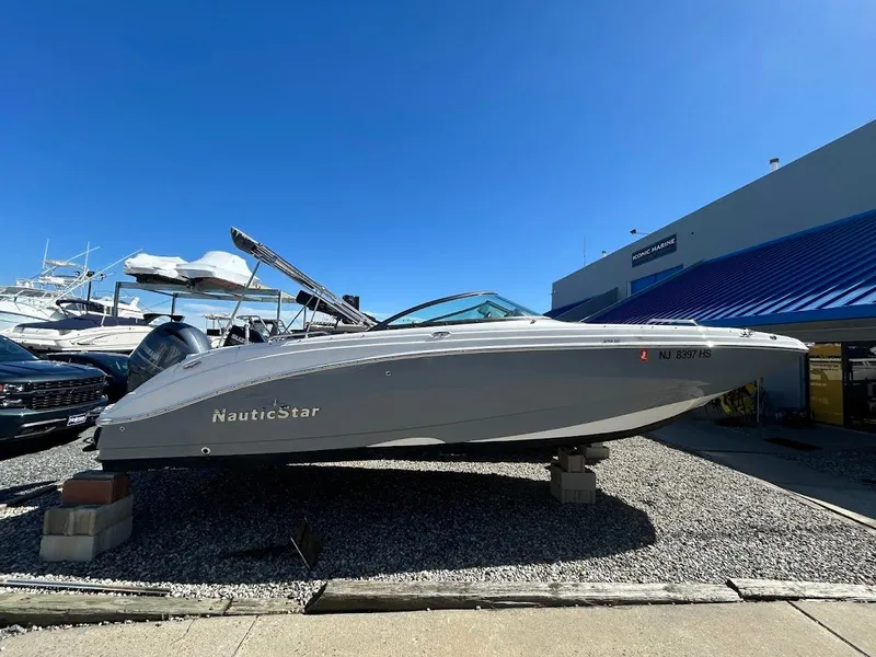 The Image of 2022 NauticStar 243DC Sport Deck boat displayed outdoors on gravel. - 0